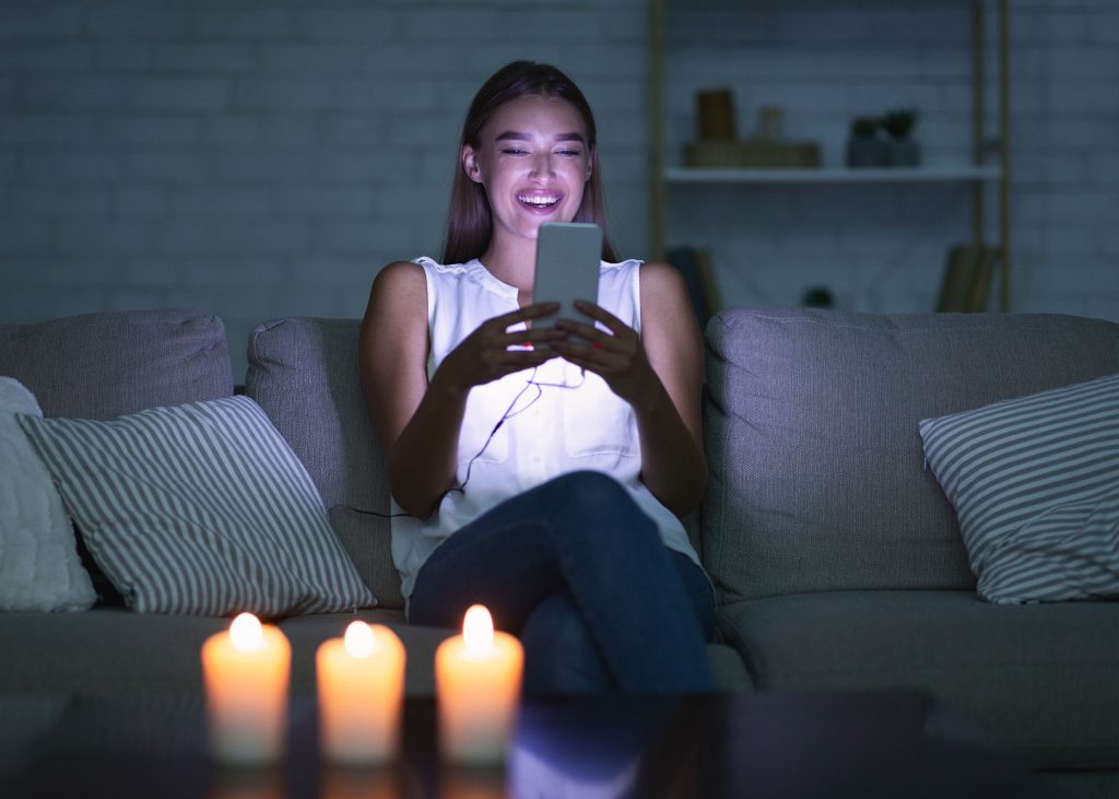 pretty girl sending a sext message in dark room with candles.